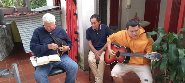 Un grupo en la finca; una persona toca guitarra mientras otra sostiene un rosario